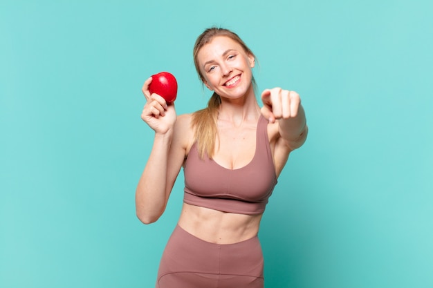 Jonge mooie sportvrouw die een appel wijst of toont en vasthoudt