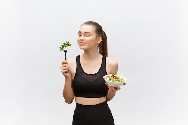 Jonge mooie sportvrouw die salade eet