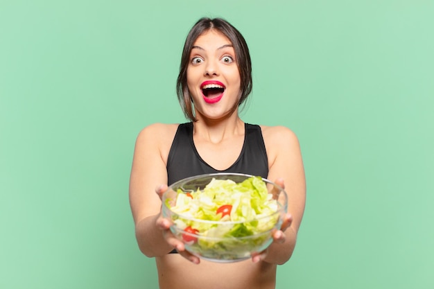 Jonge mooie sportvrouw verraste uitdrukking en houdt een salade?