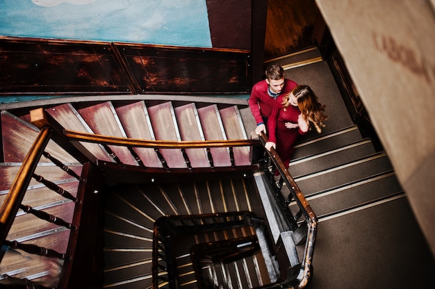 Jonge mooie stijlvolle paar in een rode jurk in grote houten vintage trappen