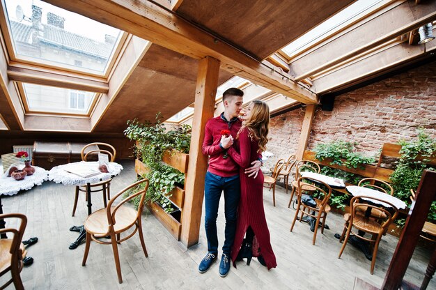 Jonge mooie stijlvolle paar in een rode jurk in liefdesverhaal in het vintage café met grote ramen op het dak