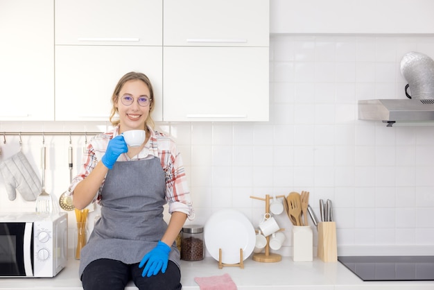 Jonge, mooie stijlvolle vrouw die een witte mok vasthoudt in de witte keuken na het klemmen, Jonge vrouw die ontspant,