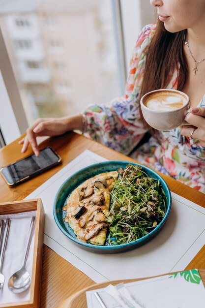 Foto jonge mooie stijlvolle vrouw die koffie drinkt terwijl ze in een restaurant zit en een smakelijk gerecht eet