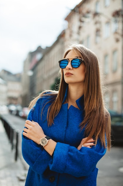 Jonge, mooie stijlvolle vrouw die op straat loopt in de herfstmodetrend van de blauwe jas