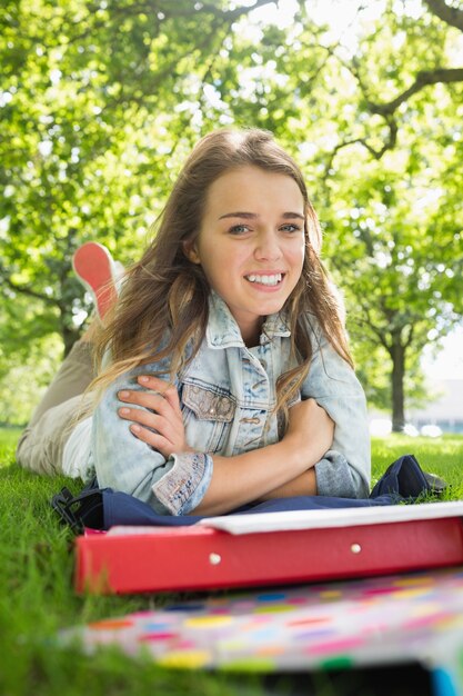 Jonge mooie student die op het gras ligt dat bij camera glimlacht