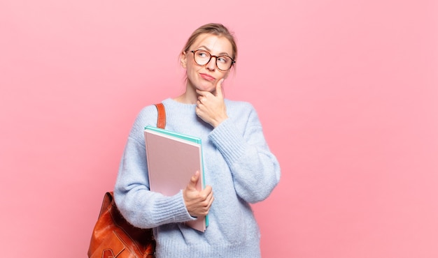 jonge mooie student glimlachend met een gelukkige, zelfverzekerde uitdrukking met de hand op de kin, zich afvragend en opzij kijkend