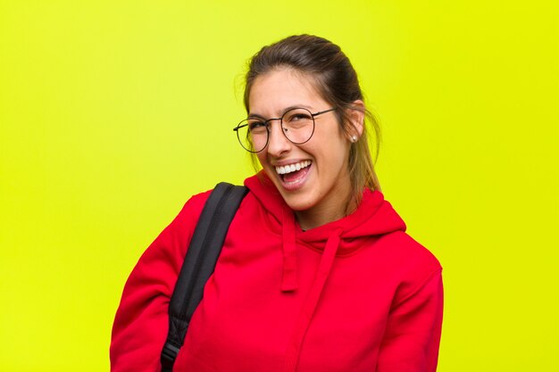 Jonge mooie student met een grote, vriendelijke, zorgeloze glimlach, die er positief, ontspannen en gelukkig uitziet, chillen