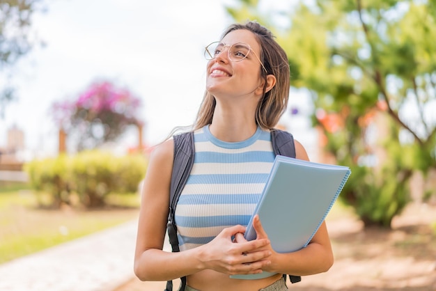 Jonge mooie student vrouw buiten opkijkend terwijl ze glimlacht