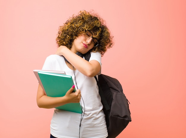 Jonge mooie student vrouw gevoel verliefd, glimlachend, knuffelen en knuffelen zelf, single blijven, egoïstisch en egocentrisch tegen roze muur