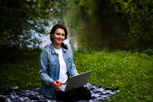 Jonge mooie studente in denim kleding werkt in het park op een laptop