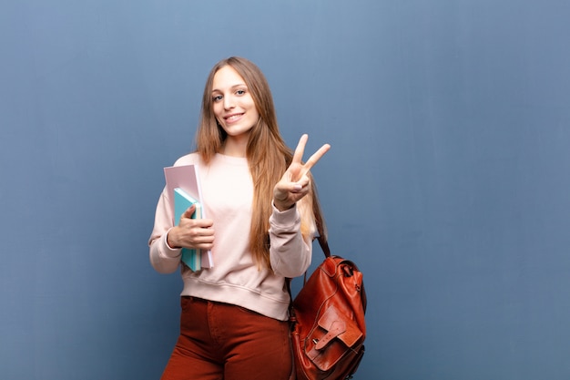 Jonge mooie studentenvrouw met boeken en zak blauwe muur met een copyspace