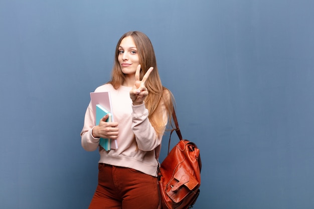 Jonge mooie studentenvrouw met boeken en zak tegen blauw met een copyspace