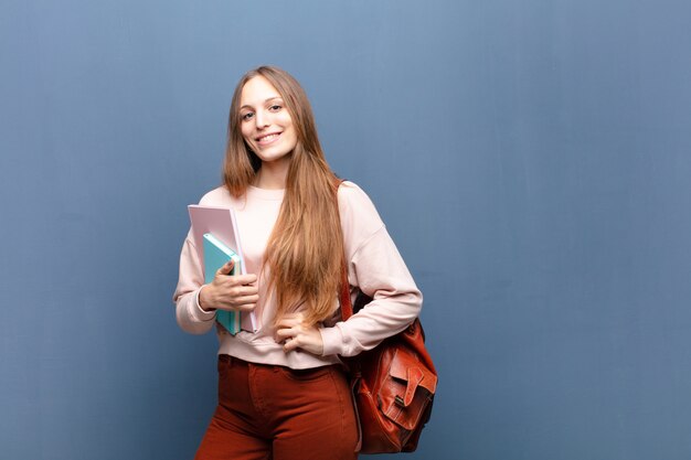 Jonge mooie studentenvrouw met boeken en zak tegen blauwe muur met een exemplaarruimte