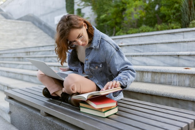 Jonge mooie studentenvrouw zit met laptop en boeken Kaukasisch meisje studeert met notebook buitenshuis