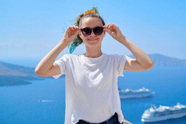 Jonge mooie tiener meisje toeristische poseren glimlachend, achtergrond zomer zonnige schilderachtige zee landschap met witte cruiseschepen in de Egeïsche Zee op het beroemde Griekse eiland Santorini