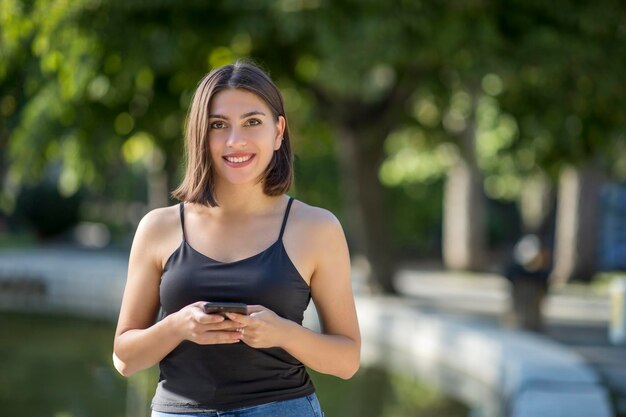 Jonge mooie Turkse vrouw controleert mobiele telefoon terwijl ze lacht en ze kijkt naar de camera