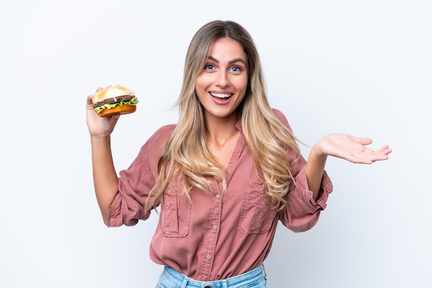 Jonge mooie Uruguayaanse vrouw met een hamburger geïsoleerd op een witte achtergrond met geschokte gelaatsuitdrukking