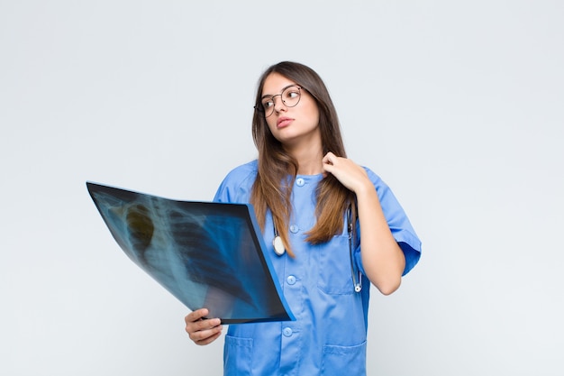 Jonge mooie verpleegster die zich gestrest, angstig, moe en gefrustreerd voelt, aan de hals van het shirt trekt, gefrustreerd kijkt door het probleem