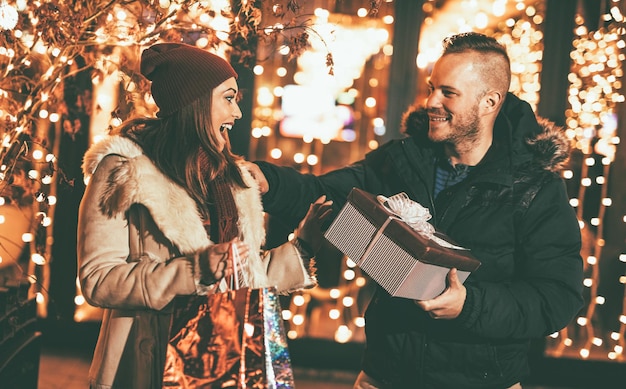 Jonge mooie vrolijke paar vieren Kerstmis in de straat van de stad en geven veel cadeau aan elkaar.