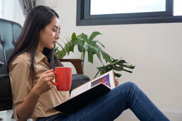 Jonge mooie vrouw Aziatische witte huid zitten drinken koffie en het lezen van een boek geniet van rust