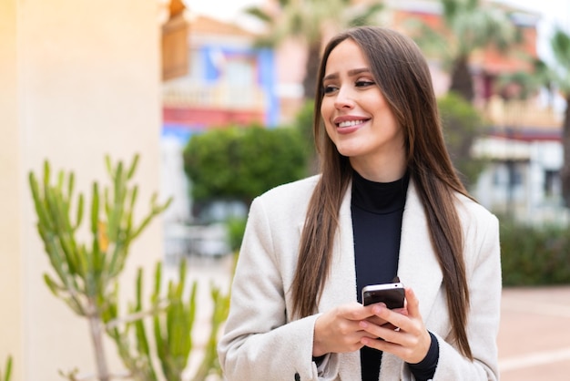 Jonge mooie vrouw buitenshuis met behulp van mobiele telefoon en opzoeken