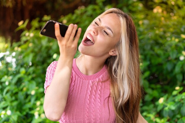 Jonge mooie vrouw buitenshuis met behulp van mobiele telefoon en zingen