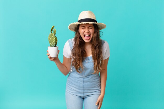 Jonge mooie vrouw die agressief schreeuwt, erg boos kijkt en een cactus vasthoudt