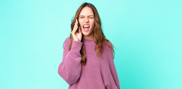 Jonge mooie vrouw die agressief schreeuwt, erg boos kijkt en een smartphone gebruikt