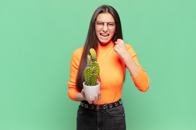 Jonge mooie vrouw die agressief schreeuwt met een boze uitdrukking of met gebalde vuisten om succes te vieren. cactusconcept