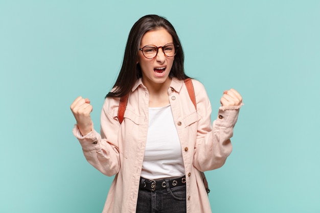 Jonge mooie vrouw die agressief schreeuwt met een boze uitdrukking of met gebalde vuisten om succes te vieren. studentenconcept