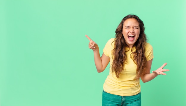 Jonge mooie vrouw die boos, geïrriteerd en gefrustreerd kijkt en naar de kopieerruimte wijst