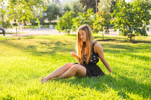 Jonge mooie vrouw die buiten van muziek geniet op een koptelefoon die op het gras ligt en er gelukkig uitziet