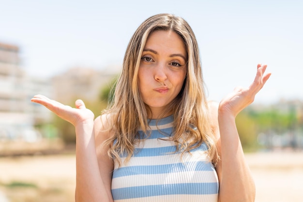 Jonge mooie vrouw die buitenshuis twijfelt terwijl ze haar hand opsteekt