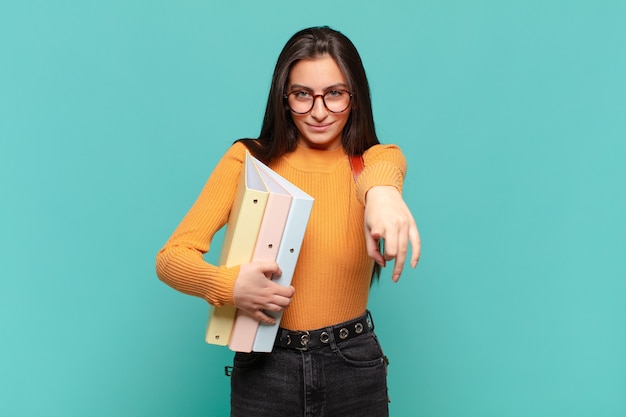 Jonge mooie vrouw die direct wijst met een tevreden, zelfverzekerde, vriendelijke glimlach en jou kiest. studentenconcept