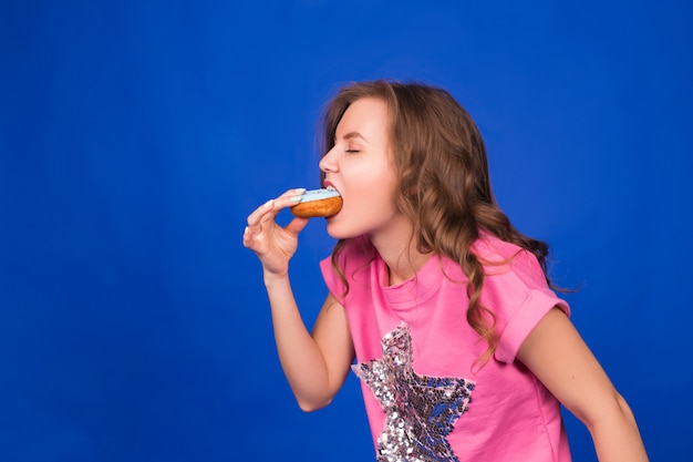 Jonge mooie vrouw die donuts op blauw eet.