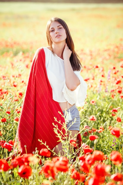 Jonge mooie vrouw die door een papavergebied loopt in de zomer. Portret van mooie jonge romantische vrouw poseren op veld close-up. Zachte kleuren.