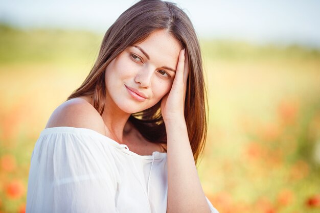 Jonge mooie vrouw die door een papavergebied loopt in de zomer. Portret van mooie jonge romantische vrouw poseren op veld close-up. Zachte kleuren.