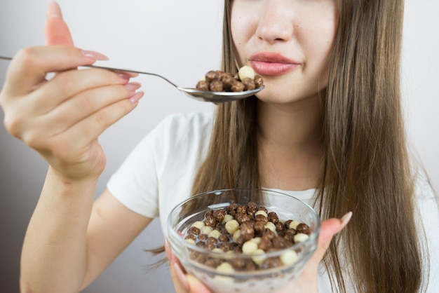 Foto jonge mooie vrouw die droge ontbijtballen met melk eet.