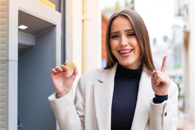 Jonge mooie vrouw die een Bitcoin in de open lucht vasthoudt en een geweldig idee benadrukt