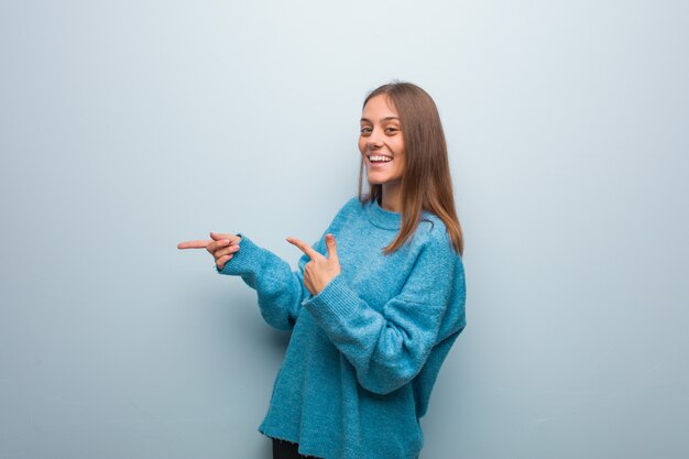 Jonge mooie vrouw die een blauwe sweater draagt die aan de kant met vinger richt