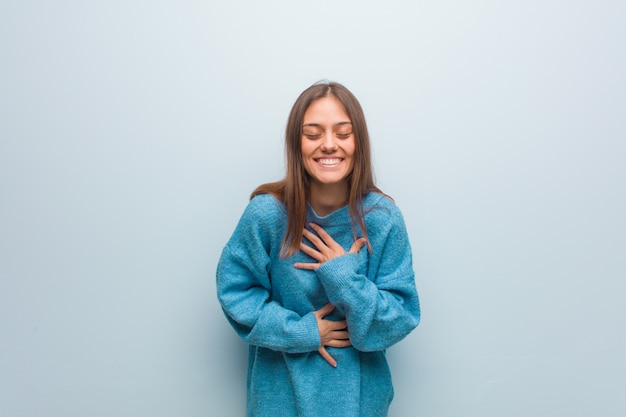 Jonge mooie vrouw die een blauwe sweater draagt die en pret lacht heeft