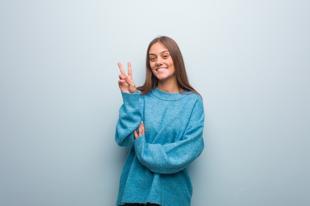 Jonge mooie vrouw die een blauwe sweater draagt die nummer twee toont