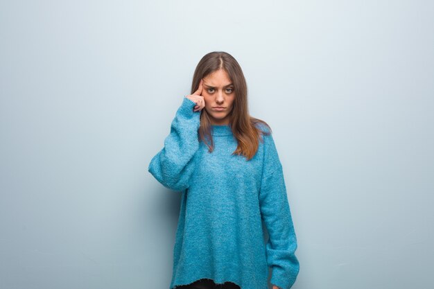 Jonge mooie vrouw die een blauwe sweater draagt die over een idee nadenkt