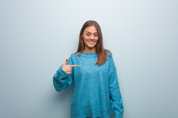 Jonge mooie vrouw die een blauwe sweaterpersoon draagt die met de hand naar de ruimte van een overhemdskopie wijst, trots en zelfverzekerd