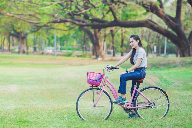 Jonge mooie vrouw die een fiets in een park berijdt.