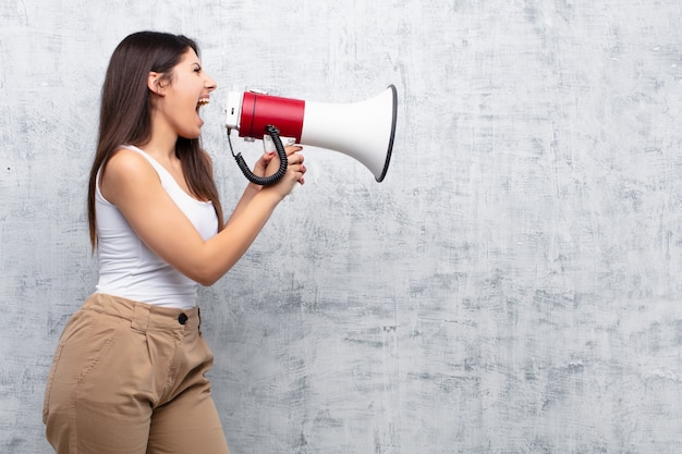 Jonge mooie vrouw die een megafoon houdt tegen cementmuur