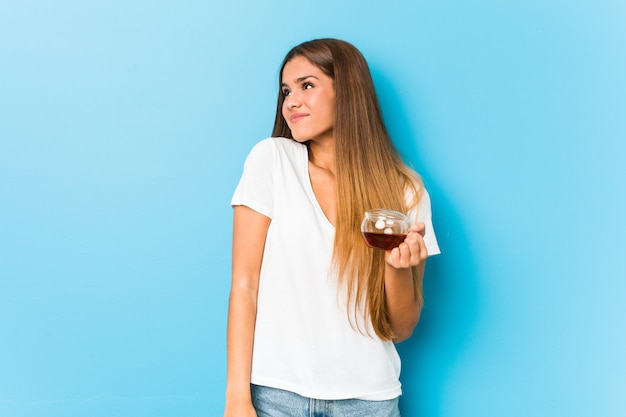 Jonge mooie vrouw die een theekop houdt die van het bereiken van doelstellingen en doeleinden droomt