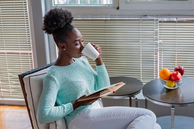 Jonge mooie vrouw die en koffie zitten drinken terwijl het lezen van een boek