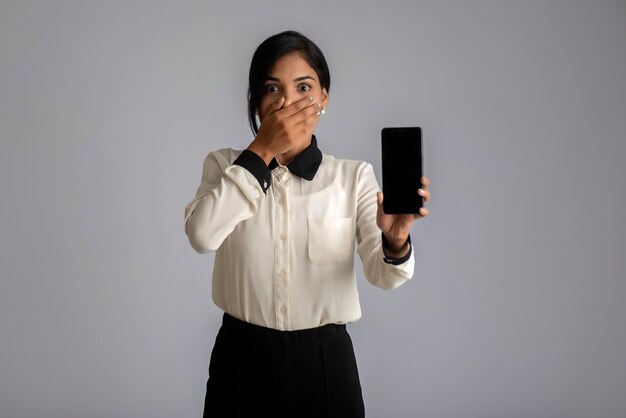 Jonge mooie vrouw die en leeg scherm smartphone of gsm of tablet telefoon op een grijze muur houdt.