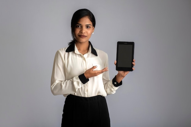 Jonge mooie vrouw die en leeg scherm smartphone of gsm of tablet telefoon op een grijze muur houdt.